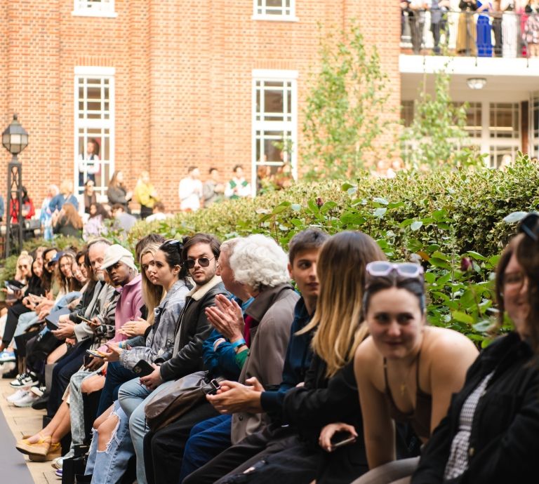 A group of people sit on the sidelines of the Quad fashion catwalk.